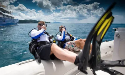 Northern Sun: Two divers in scuba gear sitting on an inflatable boat edge with fins, a yacht in the distance