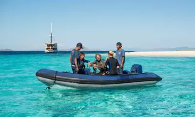 Ocean Pure: ターコイズ色の浅瀬を進む、クルーとゲストを乗せたインフレータブルのテンダー。遠くにヨットが錨泊している