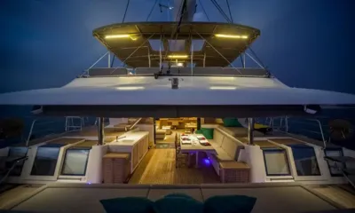 Ocean Views: Stern view at night of the lit cockpit, dining table and saloon under a hardtop