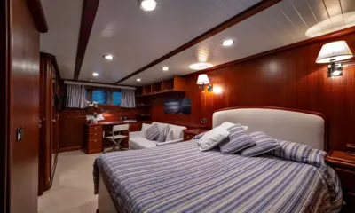 Persuader: Cabine com painéis de madeira, cama de casal, roupa de cama listrada, sofá, escrivaninha e luminárias de parede