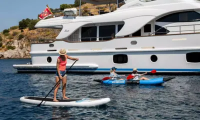 Rebecca V: Mulher em um paddleboard e duas pessoas em um caiaque inflável ao lado de um iate branco