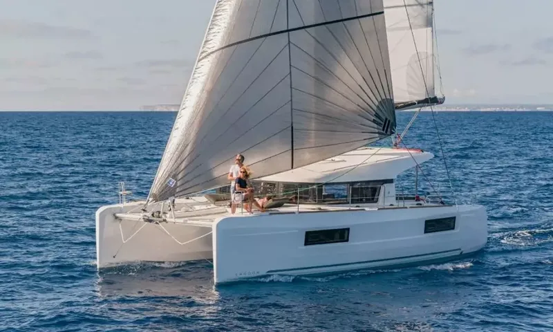 Grande: White sailing catamaran under full sail on blue sea with two people standing on the foredeck