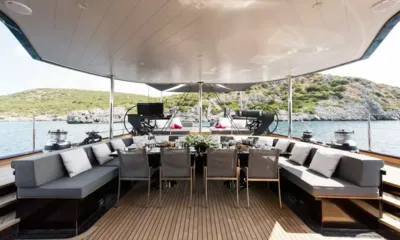 Rox Star: Tavolo da pranzo coperto sul ponte di poppa con divani grigi e sedie, colline e mare sullo sfondo