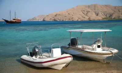 Samata: Two tenders moored on a sandy shore with the anchored yacht and dry hills behind