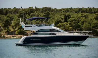 Splendid: Perfil lateral de um iate a motor com casco azul marinho e bimini do flybridge ancorado perto de uma costa arborizada