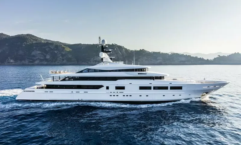Suerte: Side profile of a white superyacht under way beside a hilly coastline