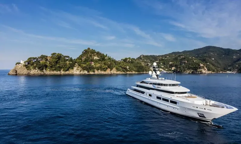 Suerte: White superyacht heading out to sea past a rocky wooded headland