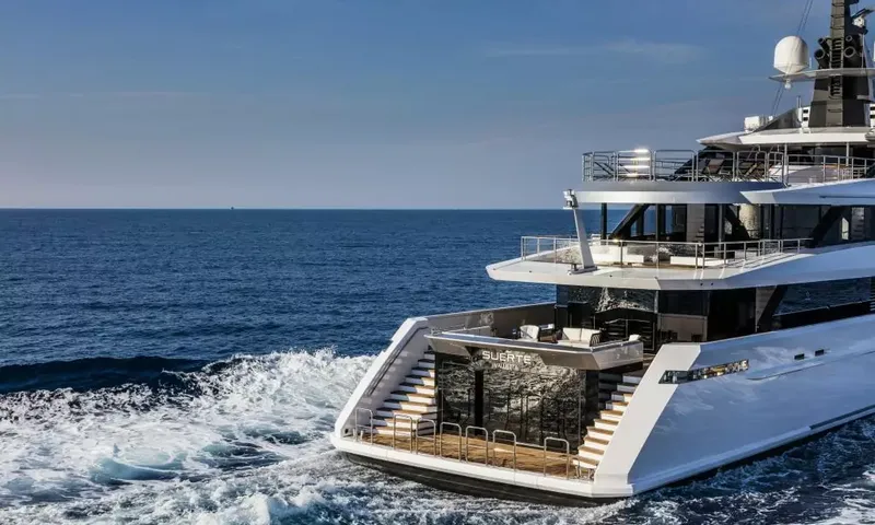 Suerte: Stern of a yacht under way with twin staircases down to a swim platform