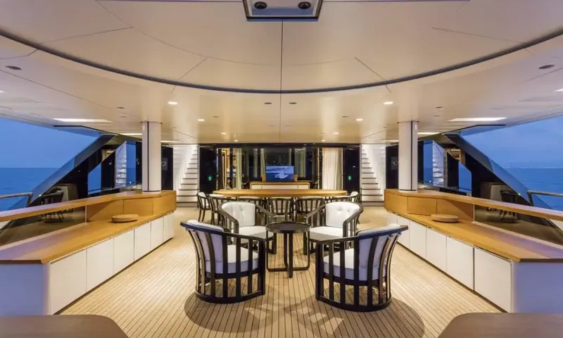 Suerte: Covered aft deck with armchairs, a long dining table and teak flooring at dusk