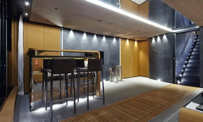 Suerte: Lounge area with a high bar table, dark stools and lit staircase