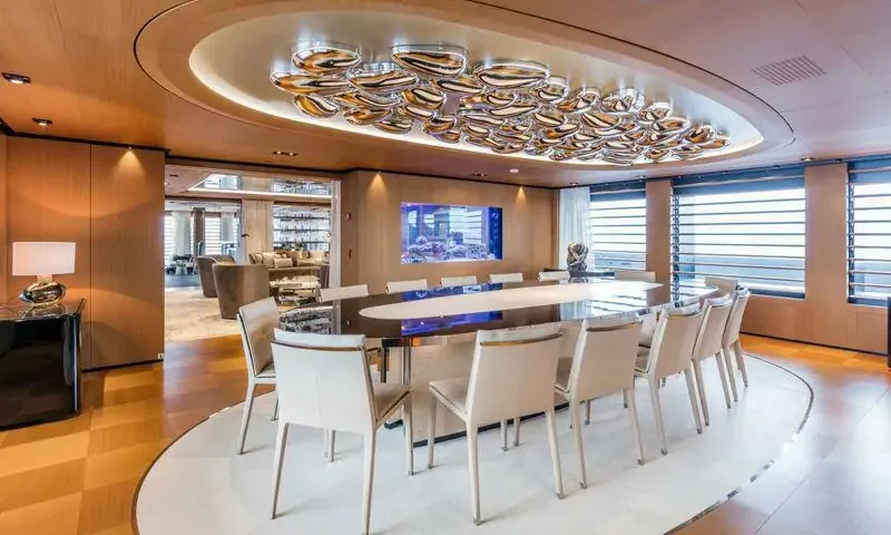 Suerte: Oval dining table with cream chairs under a sculptural ceiling light, aquarium in the wall