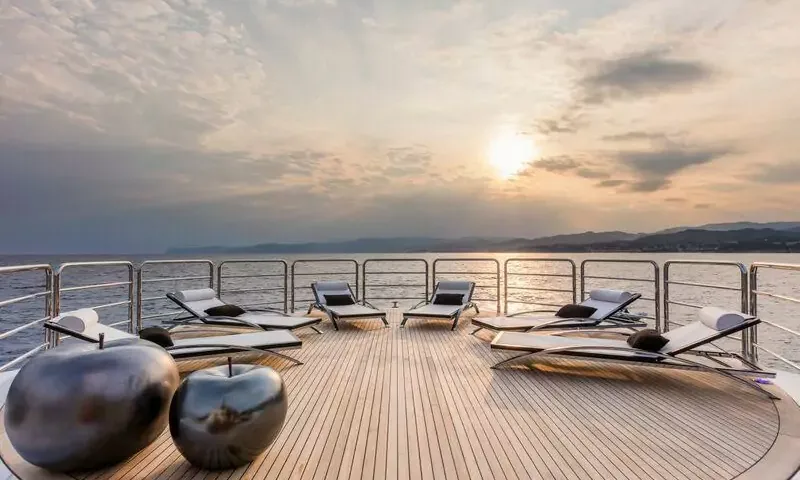 Suerte: Teak deck with sun loungers and decorative apple sculptures facing a sunset over the sea