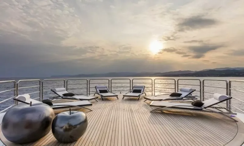 Suerte: Teak deck with sun loungers and decorative apple sculptures facing a sunset over the sea
