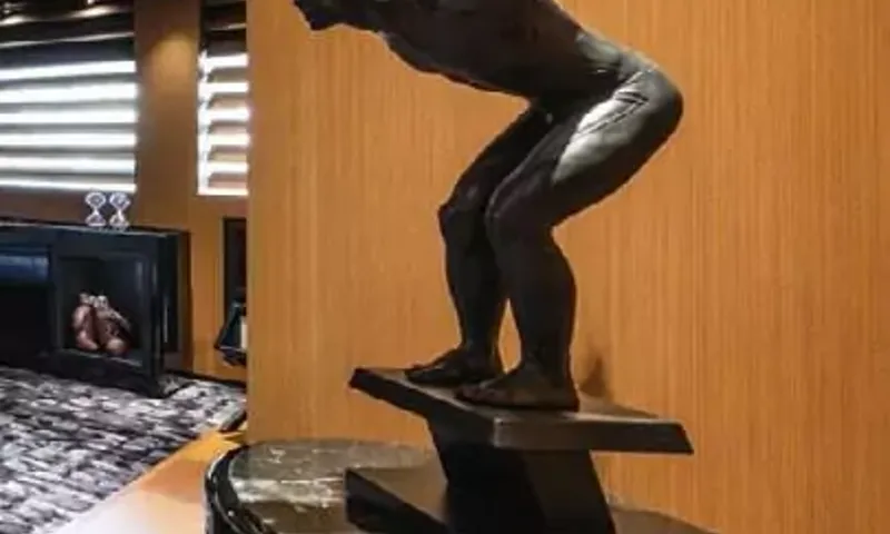 Suerte: Dark bronze sculpture of a diver poised on a plinth against wood panelling