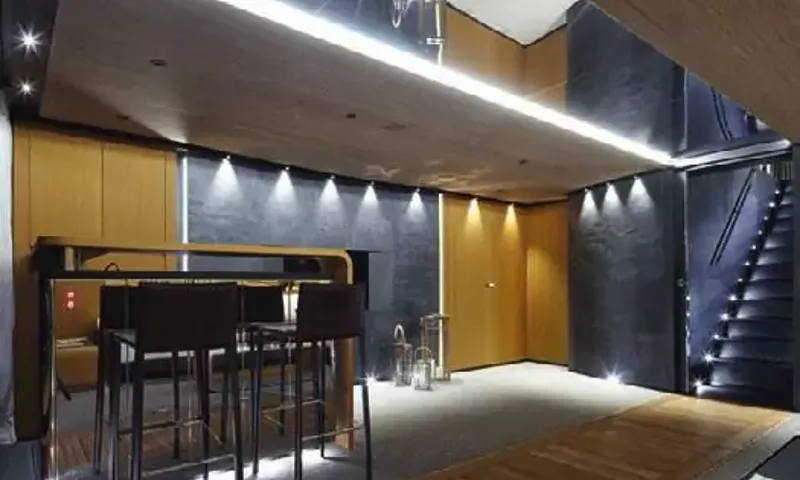 Suerte: Dimly lit lounge area with bar stools, dark stone walls and an illuminated staircase