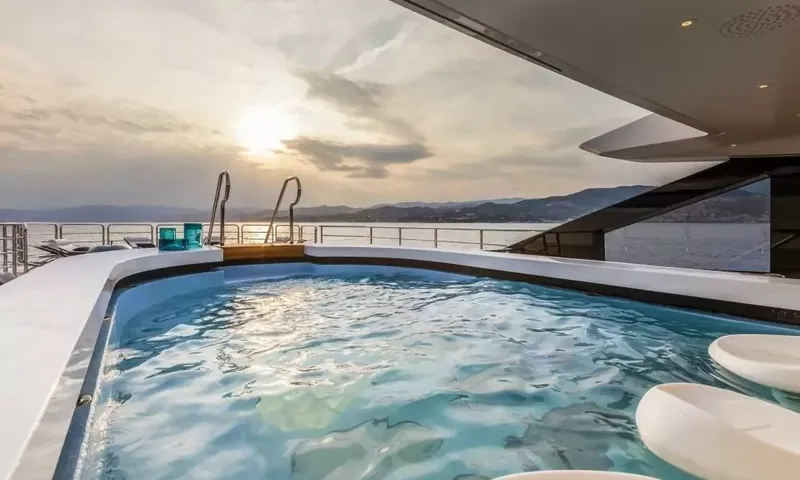 Suerte: Deck pool with clear water and ladders, coastline and setting sun beyond