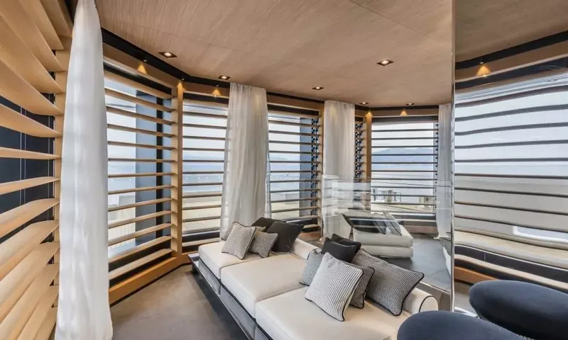 Suerte: Small lounge with white sofa and cushions surrounded by slatted windows and sheer curtains