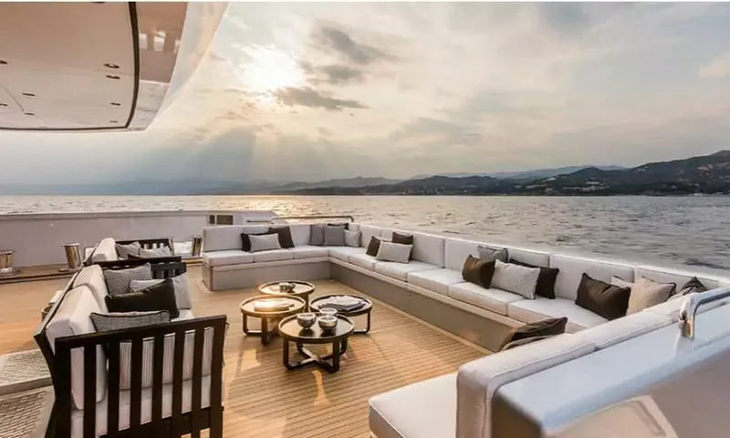 Suerte: Open teak deck with long cushioned sofas and round tables at sunset by the coast