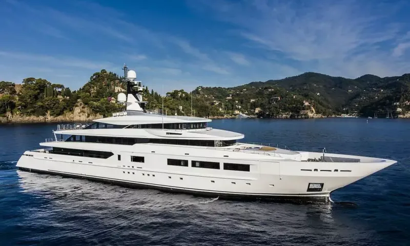 Suerte: White superyacht profile on blue water in front of green wooded hills