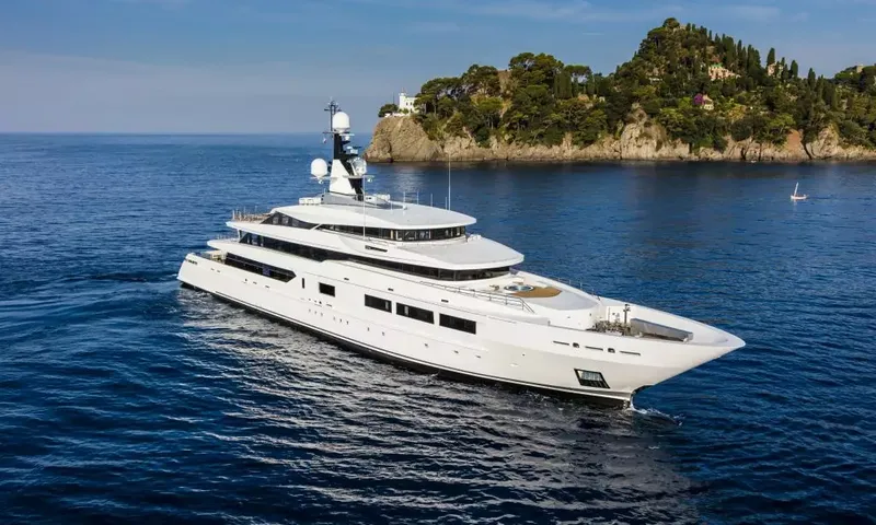 Suerte: White superyacht under way near a wooded rocky headland