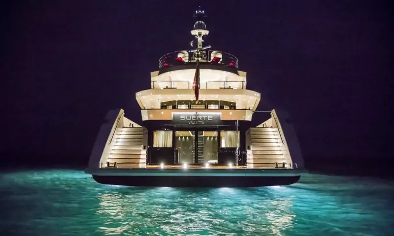 Suerte: Stern of the yacht lit at night with twin staircases and glowing turquoise water
