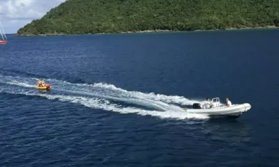 Suite Life: Bote auxiliar inflável rebocando pessoas em uma boia amarela por águas azul-escuras perto de uma ilha verde