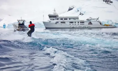 Suri: Pessoa praticando esqui aquático atrás de um barco perto do iate entre montanhas nevadas e geladas