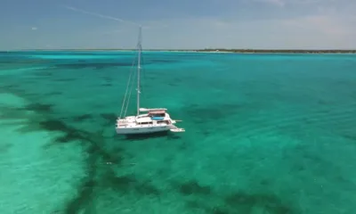 Tiger Lily: Sailing catamaran anchored in clear turquoise shallows with a distant low coastline