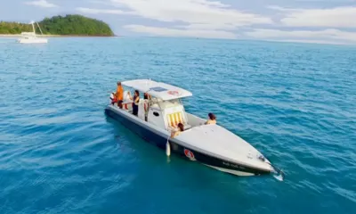 X2K: Vista de drone do barco em águas azuis calmas com convidados a bordo perto de uma ilha