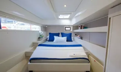 Billy: Cabine dupla com roupa de cama branca, almofadas azuis, janela no casco e escotilha no teto