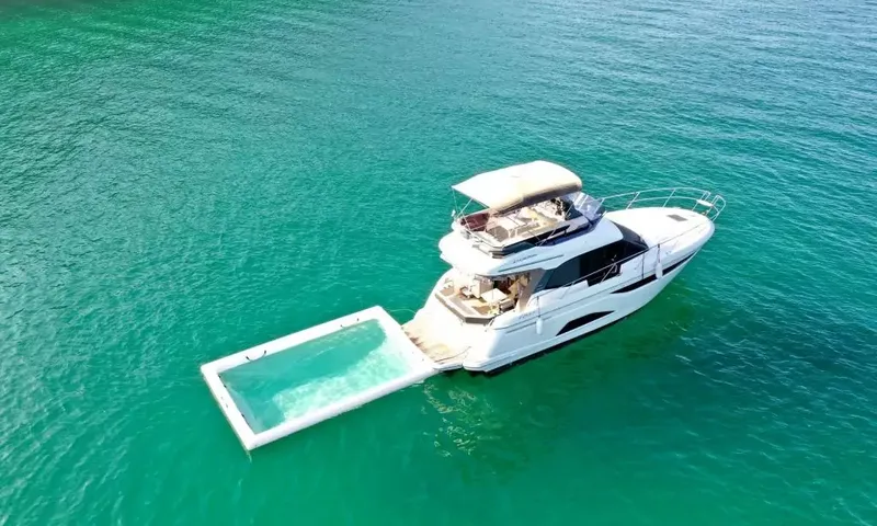 Bavaria Fly: Flybridge motor yacht from above on turquoise water with an inflatable sea pool off the stern