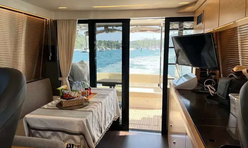 Bavaria Fly: Saloon with a covered table, snacks and television, looking aft through open doors to the sea