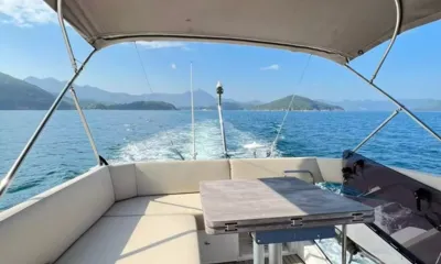 Bavaria Fly: Shaded flybridge seating and table looking aft over the wake toward green islands