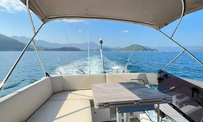 Bavaria Fly: Shaded flybridge seating and table looking aft over the wake toward green islands