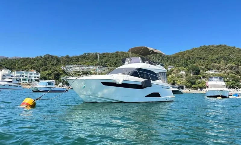 Bavaria Fly: White flybridge motor yacht moored in a bay with green hills and other boats
