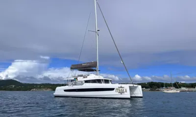 Ithaka: Catamarã a vela branco ancorado em uma baía sob um céu nublado, com colinas verdes ao fundo