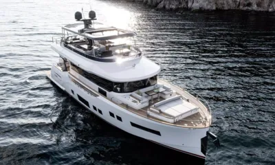 Norman's T4: Vista elevada de um iate branco com colchonete de sol no convés de proa e flybridge sombreado perto de uma costa rochosa