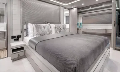 Norman's T4: Cama de casal com colcha cinza e almofadas estampadas ao lado de uma penteadeira e uma janela