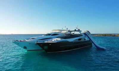 Privilegio: Two motor yachts anchored side by side in turquoise water, inflatable slide on one