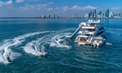 Rising Dawn: Iate ancorado com escorregador inflável, bote auxiliar ao lado e jet skis deixando esteiras por perto