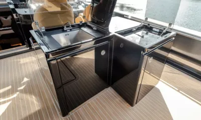 Pardo 50: Módulos de cozinha externa pretos brilhantes com pia e tampas levantadas sobre um deck de teca