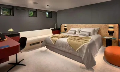 Anetta: Cabine com uma grande cama de casal, cabeceira iluminada, sofá branco, escrivaninha vermelha e pufe laranja