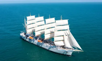 Golden Horizon: Navio a vela de cinco mastros com todas as velas brancas içadas em mar azul aberto, visto de cima