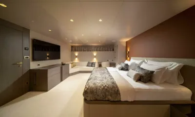 Nocturno: Cabine ampla com cama de casal, televisão na parede, cômoda e assentos de descanso sob luzes quentes