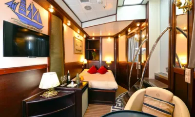 Running on Waves: Wood panelled cabin with double bed, red cushions, wall television and armchair