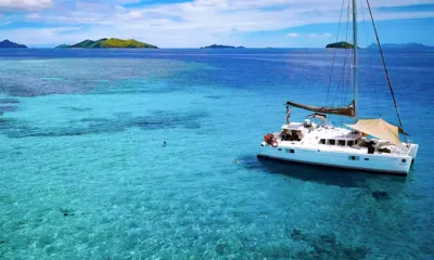 Aparima: Catamaran anchored over clear turquoise reef water with swimmers nearby and islands on the horizon