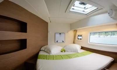 Lagoon 420: Cabine dupla com roupa de cama branca, trilho verde, parede de cabeceira de madeira e janela no casco