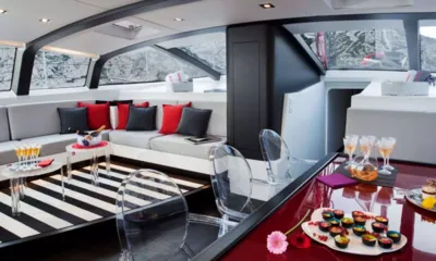 Nomad IV: Salon lumineux avec canapé gris, coussins rouges, tapis rayé et table rouge brillante avec des en-cas
