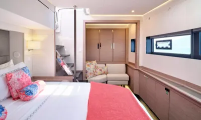 Kimata: Cabine com cama de casal, manta coral, sofá pequeno, guarda-roupa e janela no casco