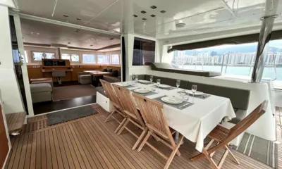 L62: Aft deck table set for eight with wooden folding chairs, saloon visible beyond